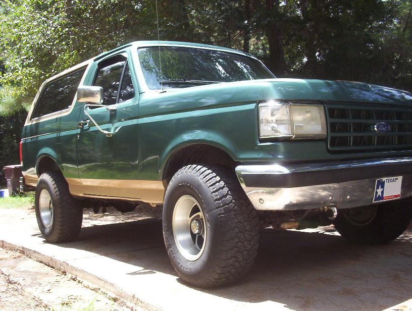 Green and tan two-tone Ford Bronco front three-quarter on shaded driveway with Texas plate