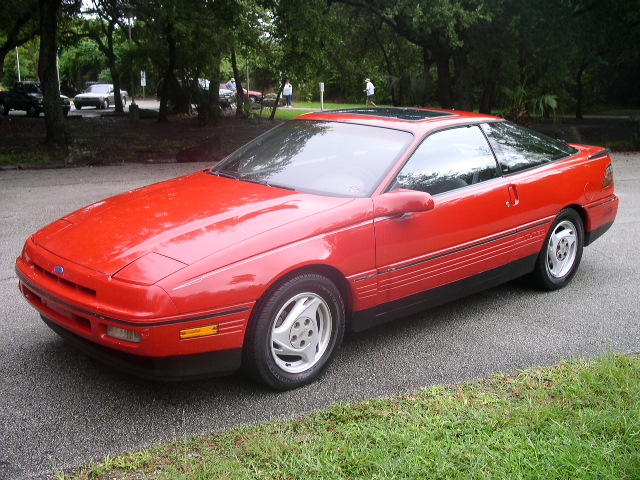 Red Ford Probe front three-quarter with open sunroof in a wooded parking area