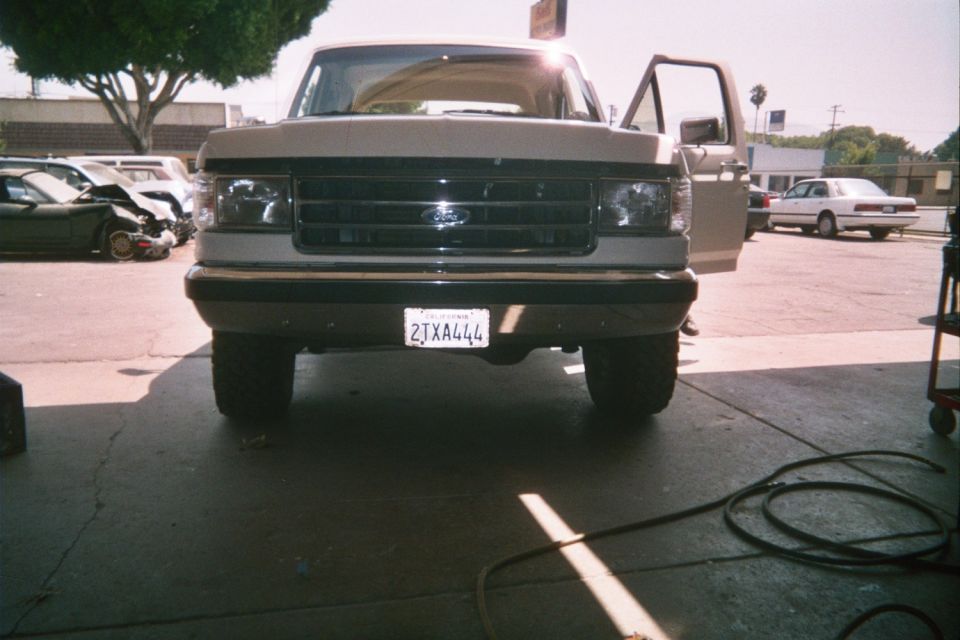 Front of a lifted tan Ford pickup with driver door open in a lot