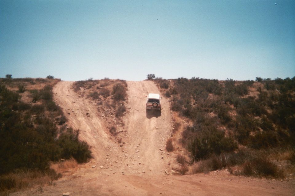 vehicle cresting a steep rutted dirt hill in dry brush country