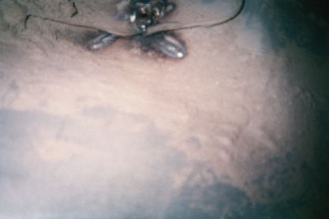 1990 Ford Bronco - Soft-focus close-up of a small welded metal bracket and wiring on a dusty underbody surface.