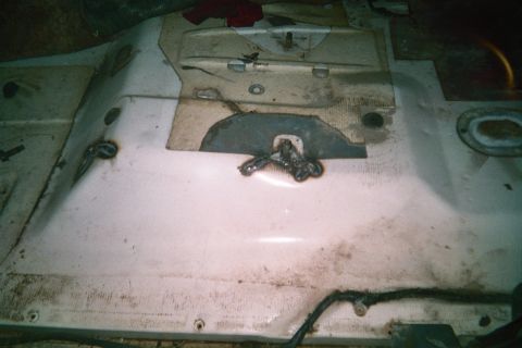 1990 Ford Bronco - welded steel tab sits on a dirty white fiberglass panel inside a vehicle interior, with bare metal and grime visible around it.