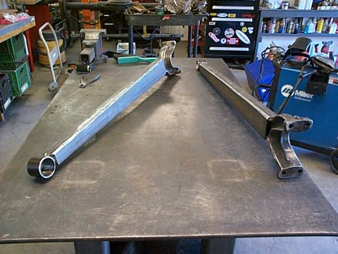 1994 Ford Bronco - Two fabricated control arms sit on a metal workbench in a workshop setting.