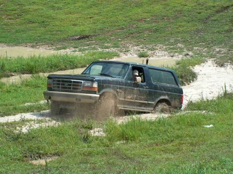 1989 Ford Bronco - Ford Bronco navigates a muddy off-road course, kicking up dirt and water.