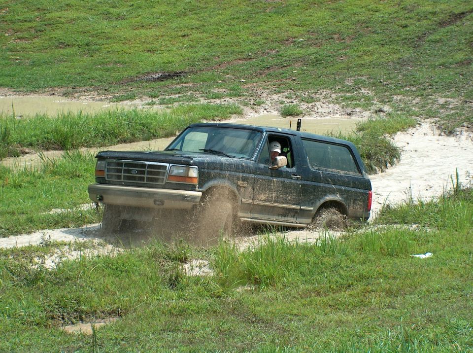 1989 Ford Bronco driving through mud puddle, splashing water