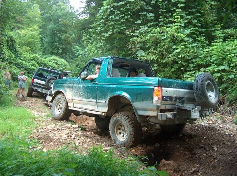 1989 Ford Bronco - Two Ford Broncos navigate a muddy, wooded trail during an off-road excursion.