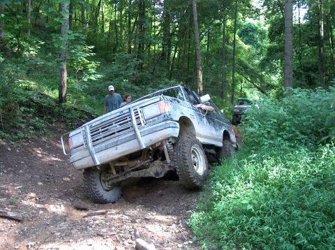 1989 Ford Bronco - Ford Bronco navigating a challenging off-road trail in a wooded area.