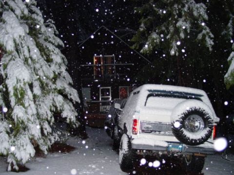 1986 Ford Bronco - Night flash photo of a white full-size SUV covered in fresh snow, seen from the rear, with a swing-out spare tire carrier holding a mud-ter…