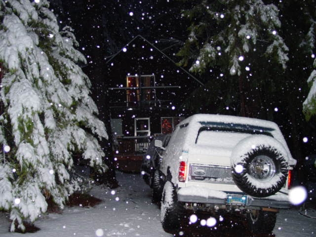 Snow-covered white SUV at night with rear swing-out spare tire carrier, snow falling