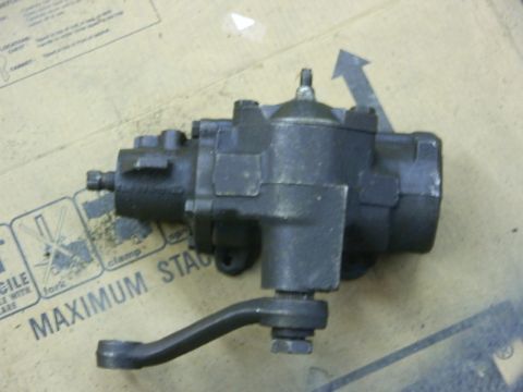 1990 Ford Bronco - A black steering gear box with a pitman arm is shown against a cardboard background with markings.