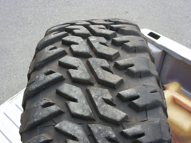 Close-up of a large off-road tire with aggressive tread pattern, sitting in the bed of a pickup truck