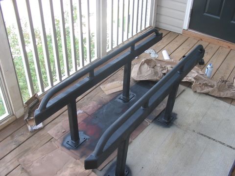 1988 Ford Bronco - A pair of black rock sliders are shown on a wooden deck, possibly after being painted.