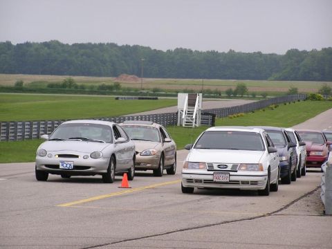 1998 Ford Taurus - A line of cars, including a silver 1998 Ford Taurus, are on a race track with an orange cone in the foreground.