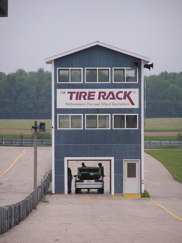 Silver sedan with open trunk parked in garage of blue building labeled "THE TIRE RACK"