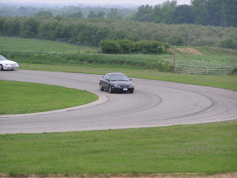 dark sedan on race track, white car in background