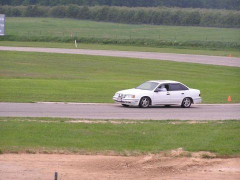 1998 Ford Taurus - A white sedan drives on a racetrack, its side profile clearly visible against the grassy infield.