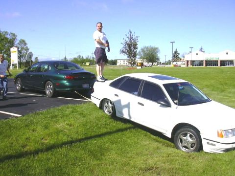 1998 Ford Taurus - A white sedan is being towed by a green sedan on a sunny day.