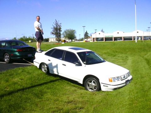 1998 Ford Taurus - A white 1998 Ford Taurus is being towed by a green sedan on a grassy area.