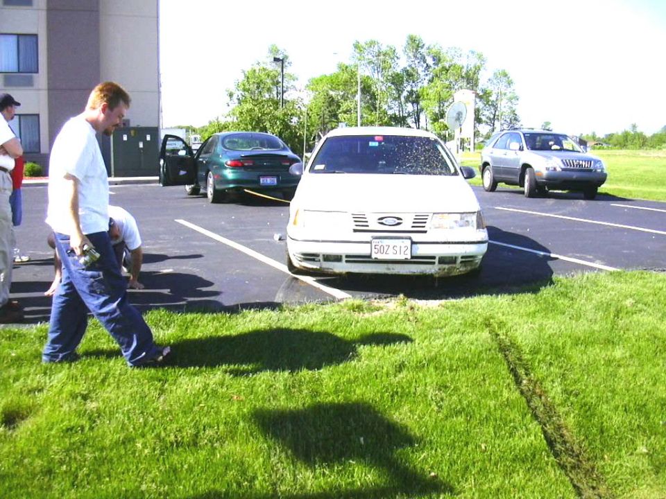 White sedan with a dented bumper and a license plate that reads 50Z S12. Green sedan and silver SUV in background