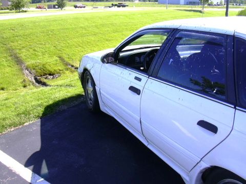1998 Ford Taurus - A white sedan is parked on asphalt next to a grassy area with visible tire tracks.