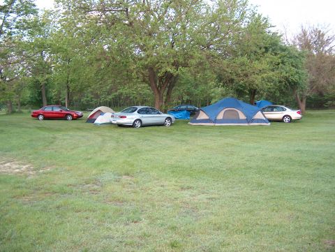 1998 Ford Taurus - A campsite scene with multiple vehicles and tents set up under trees.
