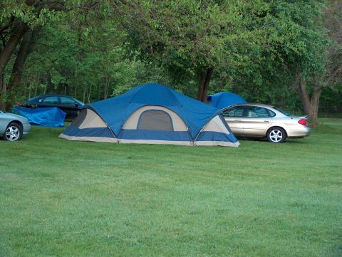1998 Ford Taurus - A campsite scene features a gold sedan and two other vehicles near tents set up on a grassy area.