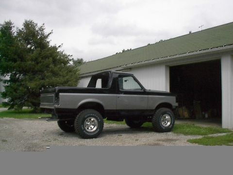 1989 Ford Bronco - Two-tone 1989 Ford Bronco with aftermarket wheels and lifted suspension parked on gravel.