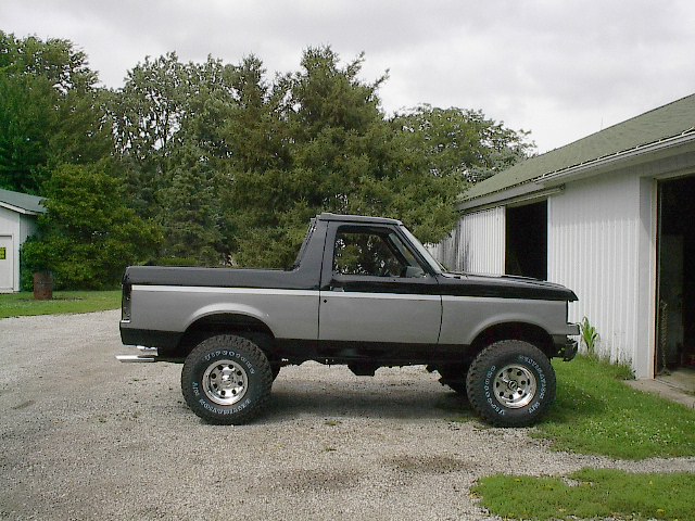 1989 Ford Bronco parked on gravel in front of a white building
