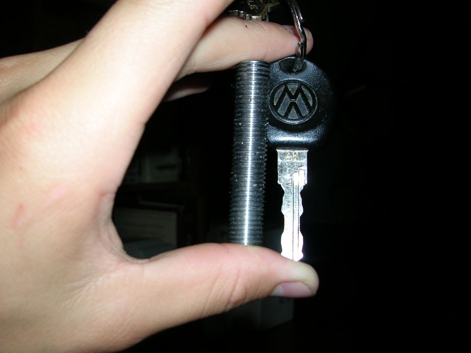 Hand holding a Volkswagen key and a threaded metal rod against a dark background