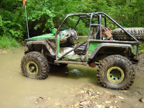 1992 Ford Bronco - Modified off-road buggy navigating a muddy water crossing with trees in the background.