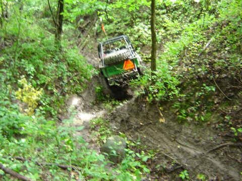 1992 Ford Bronco - An off-road vehicle navigates a steep, muddy incline surrounded by dense foliage.
