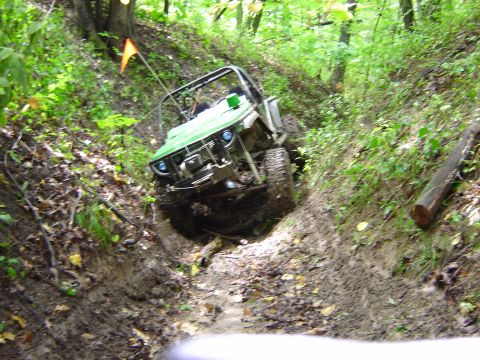1992 Ford Bronco - This green off-road vehicle navigates a challenging muddy terrain on a wooded trail.
