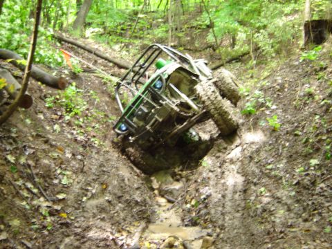1992 Ford Bronco - An off-road vehicle is stuck in a muddy ravine, its tires struggling for traction on the slippery terrain.