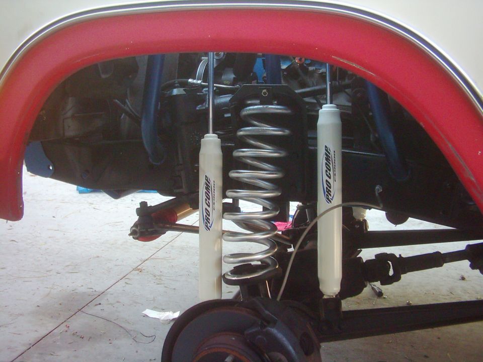 Dual white Pro Comp shocks and coil spring in the front wheel well of a lifted truck