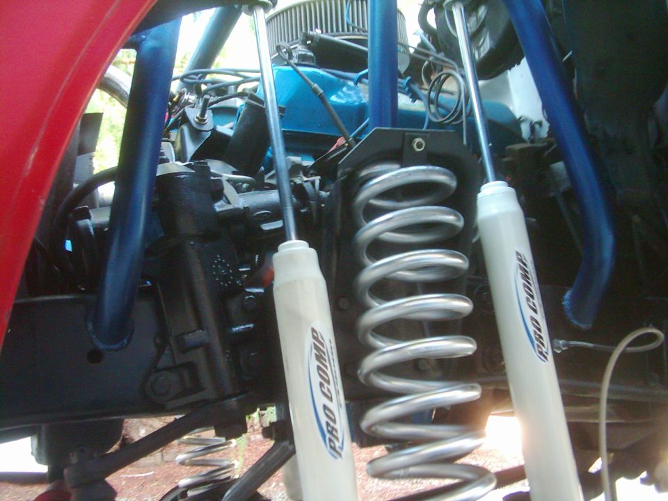 Front coil spring with white Pro Comp shocks and blue radius arms under lifted truck