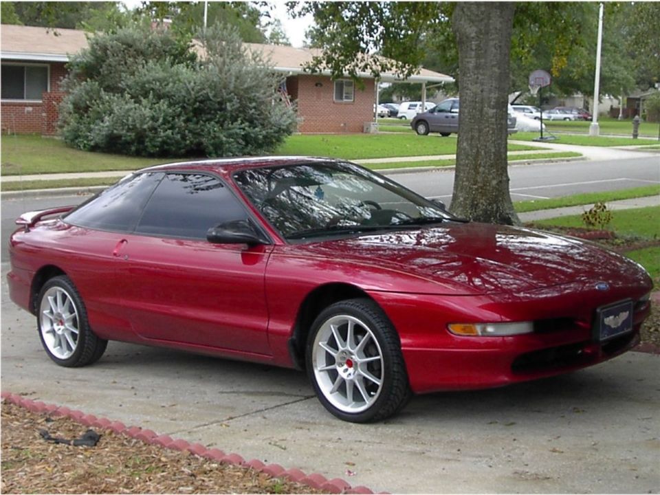 Red Ford Probe coupe with white multi-spoke wheels parked in a driveway, front three-quarter view