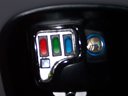 Close-up of car control panel with red, green, blue lit buttons and a chrome switch with blue ring