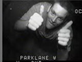 1985 Ford Bronco - Grainy black-and-white surveillance-style video still with 'PARKLANE W' burned in along the bottom, showing a grinning person leaning towar…