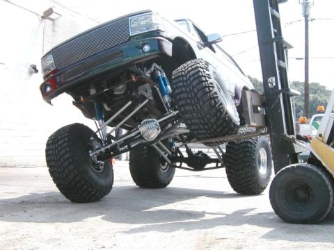 1994 Ford Bronco - Forklift lifting a heavily modified 1994 Ford Bronco with large off-road tires.