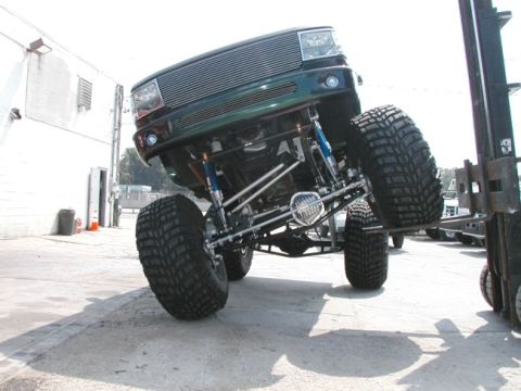 1994 Ford Bronco - This heavily modified truck features an extreme lift kit and oversized tires, with its front end elevated by a forklift.