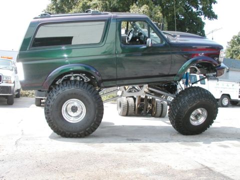 1994 Ford Bronco - A heavily modified green SUV with oversized tires and a lifted suspension is parked outdoors.