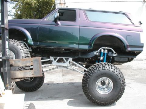 1994 Ford Bronco - This modified Ford Bronco features an extreme lift kit and oversized tires, with a forklift assisting in its maintenance.