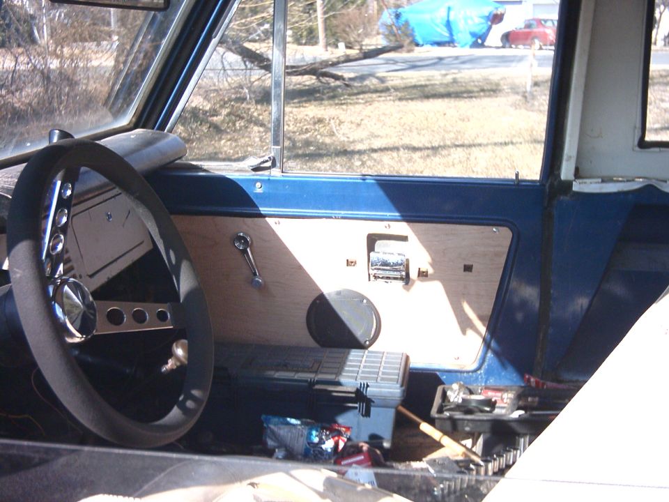 Blue Bronco interior with aftermarket steering wheel, plywood door panel, and tools on the seat