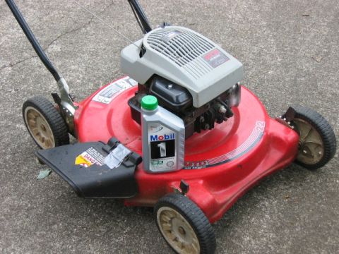 1985 Ford LTD Crown Victoria - A red lawnmower sits on a concrete surface with a bottle of Mobil 1 oil.