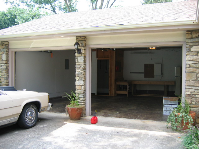 beige sedan parked in front of a two-car garage, gas can on the ground