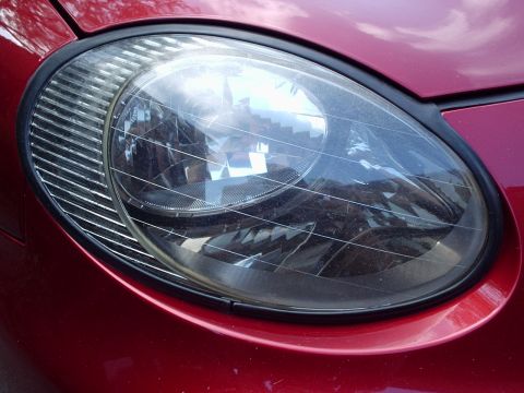 1998 Ford Taurus - Headlight assembly on a red vehicle, showing ribbed trim detail.