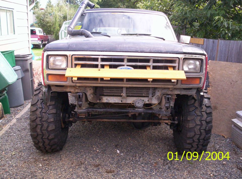 Front view of a lifted Ford Bronco with a snorkel. It has large off-road tires and a wooden plank across the grille