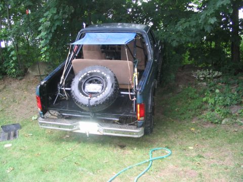 1986 Ford Bronco - The rear of a dark green 1987 Ford Bronco is visible, equipped with fishing rods and a spare tire.