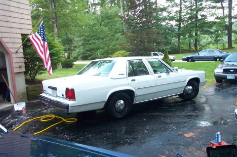 1991 Ford LTD Crown Victoria - White 1991 Ford Crown Victoria LTD parked in a wet driveway with other vehicles visible.