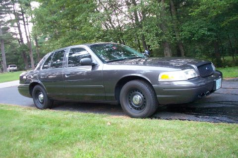 1991 Ford LTD Crown Victoria - A dark gray sedan is parked on a driveway with trees in the background.